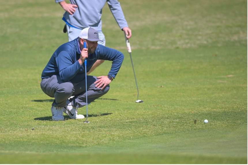 Golfer squats beside ball.