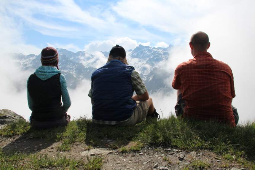 Three hikers sit at the edge of a vista