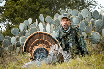 Mike Chamberlain sits in front of a large cactus with a Rio Grande wild turkey he harvested
