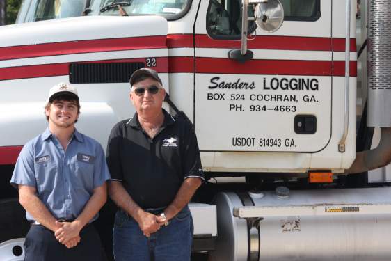Father and son loggers stand by a truck.