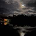A home is surrounded by water at night, with the moon reflected in the water