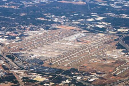 Aerial view of a large airport with multiple runways, taxiways, and terminals surrounded by urban development and roads.