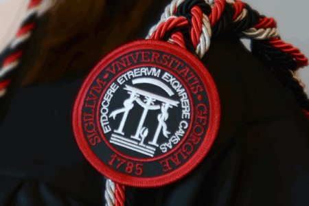 A close-up of a graduate’s black gown featuring a red, black, and white honor cord and a University of Georgia insignia patch.