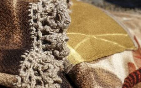 Close-up of a brown and tan patchwork blanket with a crocheted lace trim, showing various fabric textures and patterns.